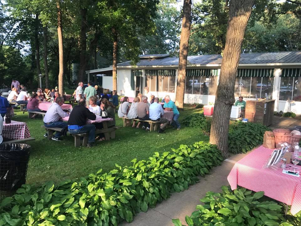 People sitting outdoors at picnic tables for a pig roast